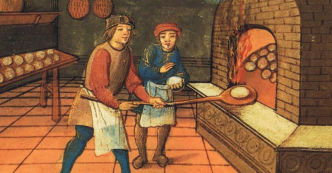 A baker and an apprentice putting an unbaked loaf of bread into a woodfired oven
