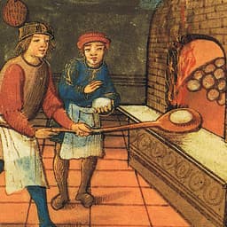 A baker and an apprentice putting an unbaked loaf of bread into a woodfired oven